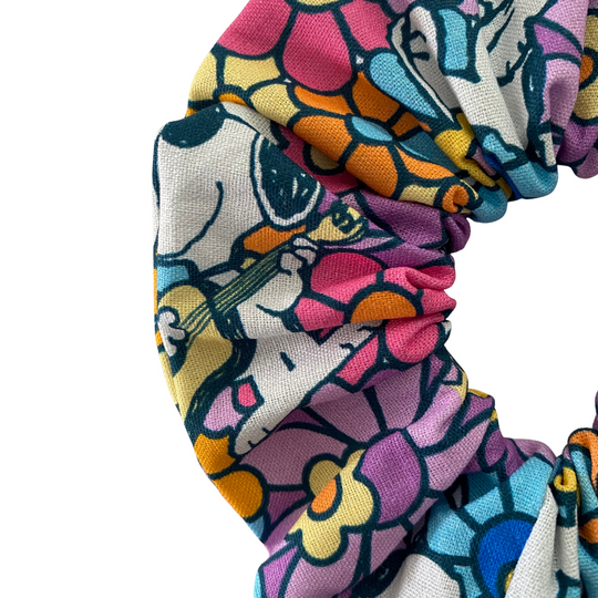 A close up view of a scrunchie with playful images of Snoopy and Woodstock on a vibrant, retro-inspired floral print.