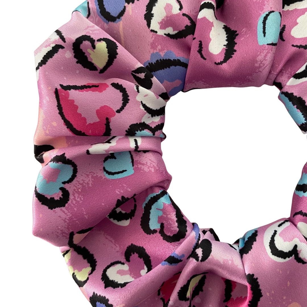 Pink scrunchie with colourful heart pattern on a white background.