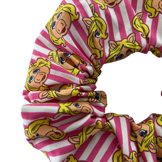 Close up view of a pink and white striped scrunchie with pig face pattern on a white background.