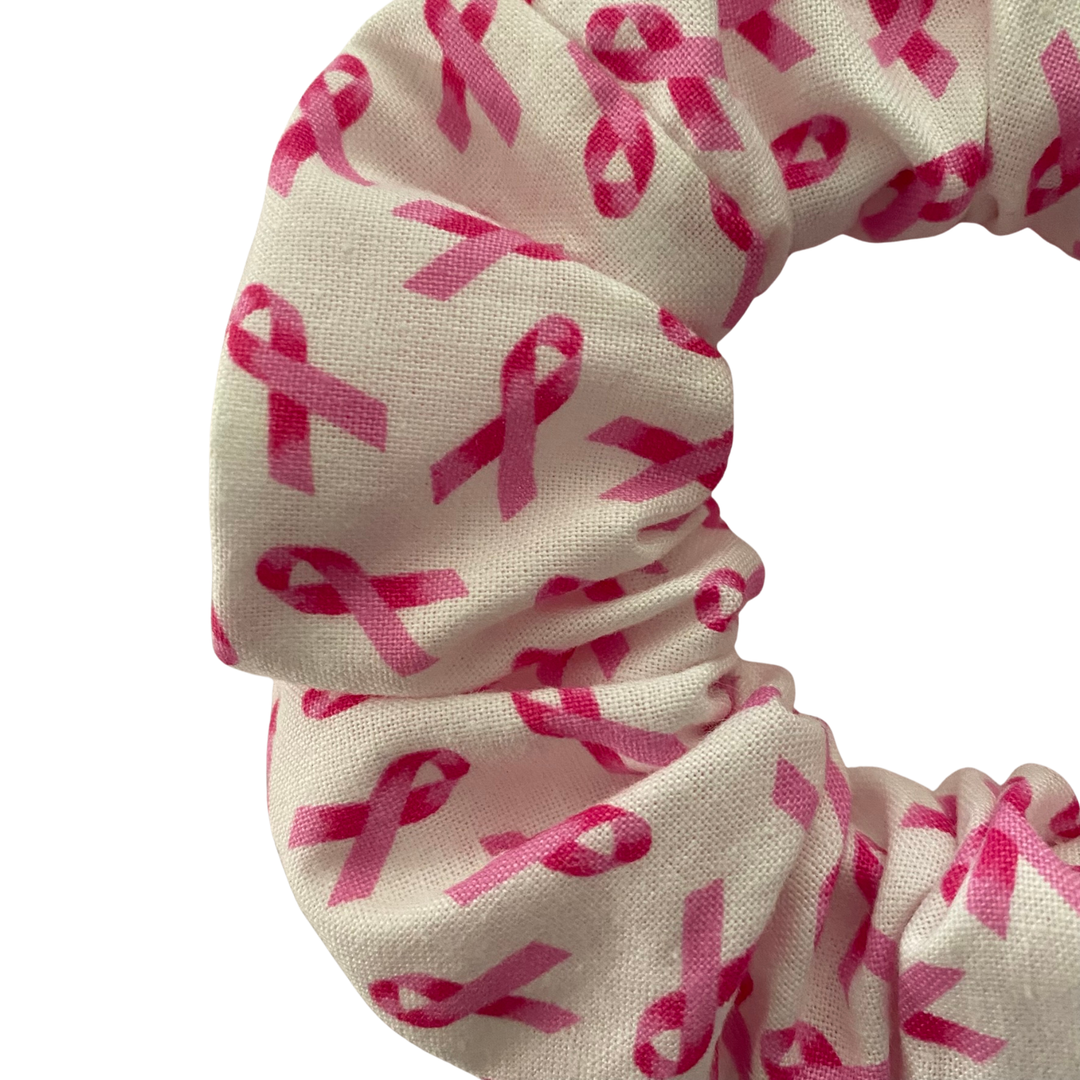 Close up view of a white scrunchie with the iconic pink ribbon symbol in a repeat print.