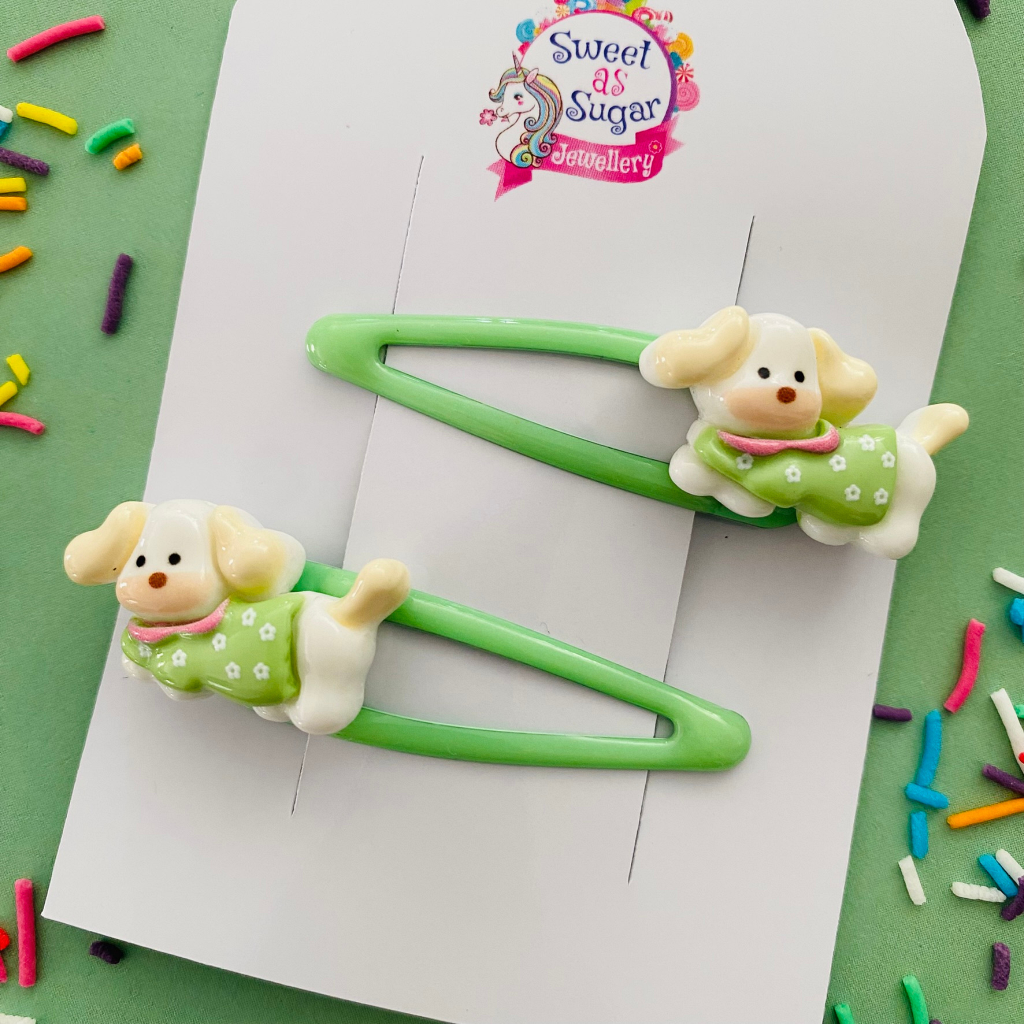 A pair of green snap clips featuring a puppy wearing a green flower jumper.