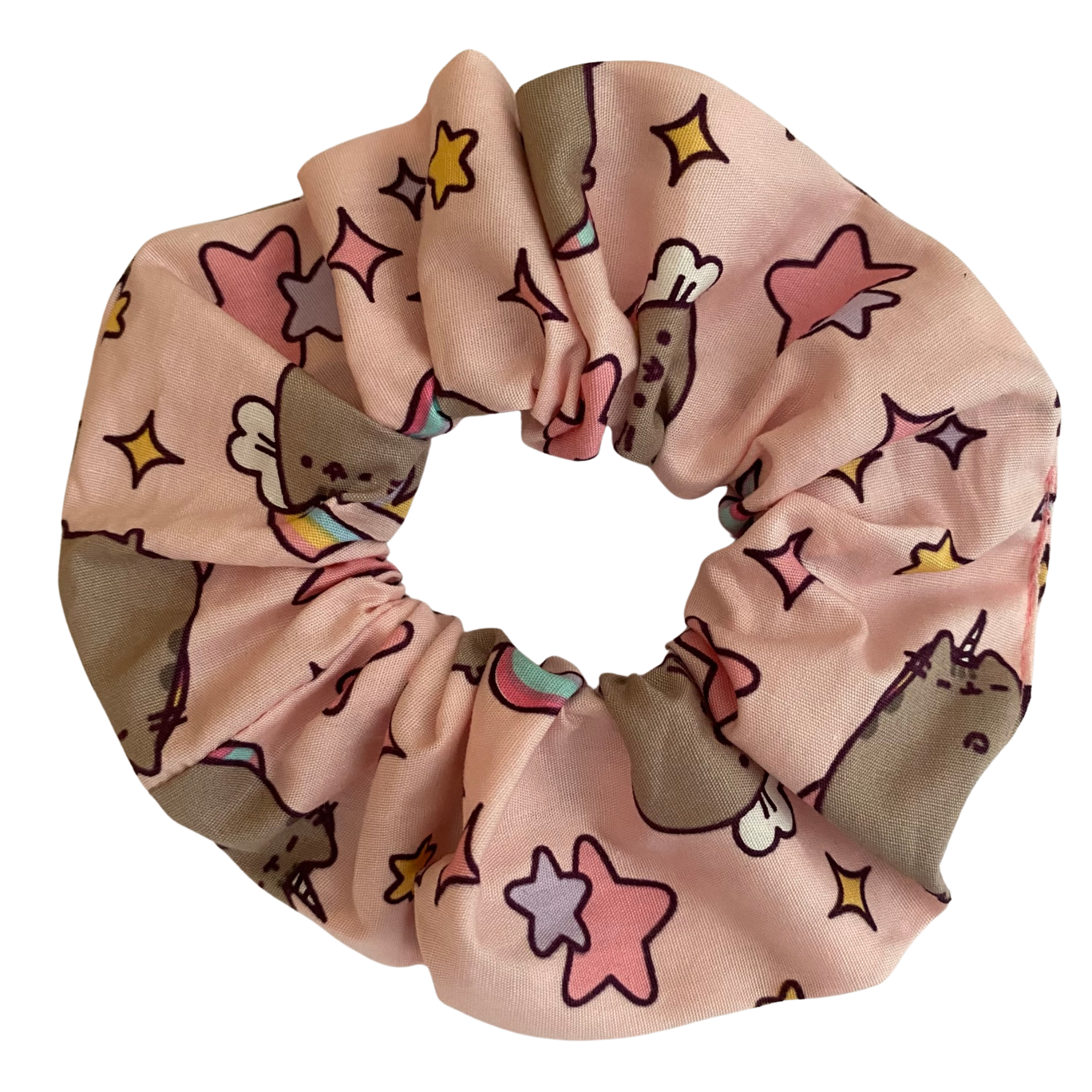 Pusheen scrunchie adorned in images of Pusheen, stars and rainbows on a light pink fabric.