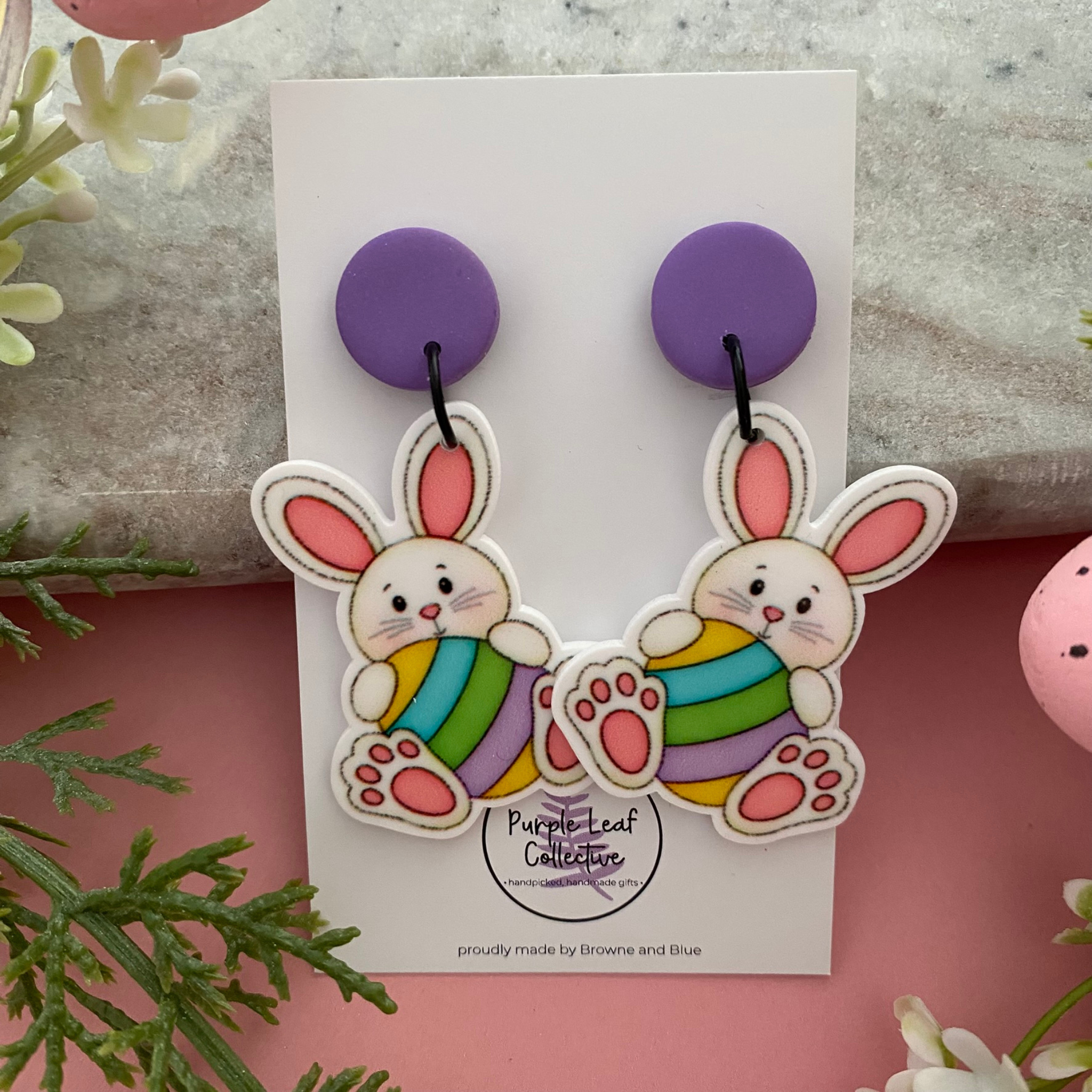 Handmade dangle earrings featuring a white rabbit silhouette holding a colorful patterned Easter egg with purple stud topper.
