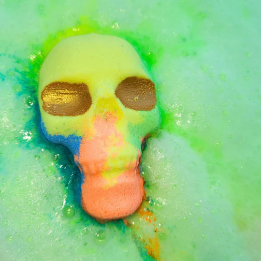 Skull bath bomb in tones of green, yellow, blue, and orange—complete with gold glitter eyes fizzing in the bath water.