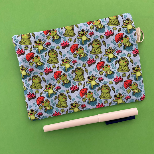 Reverse view of a zipper pouch featuring cute frogs in the rain holding umbrellas and sitting on lily pads on a crisp blue fabric.