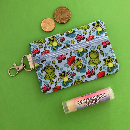 Front view of a mini pouch with images of frogs holding umbrellas and lily pads on a crisp blue fabric.