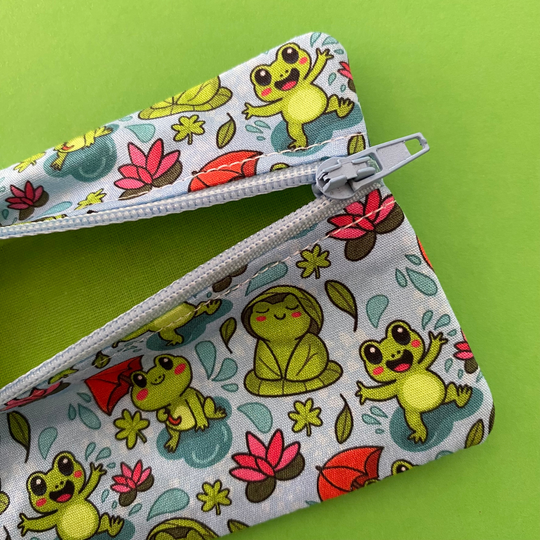 Mini pouch with images of frogs holding umbrellas and lily pads on a crisp blue fabric with lime green lining.