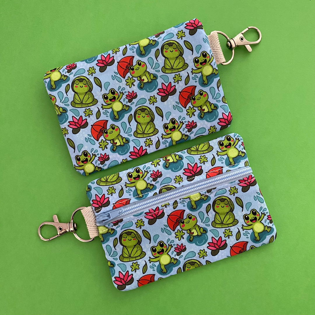 Reverse view of a mini pouch with images of frogs holding umbrellas and lily pads on a crisp blue fabric.