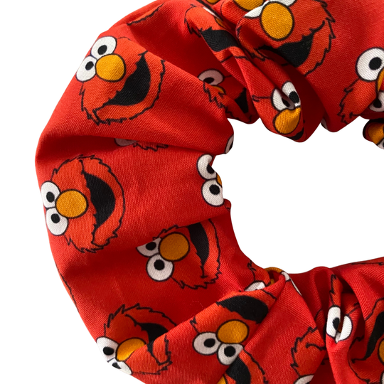 Close up view of a vibrant red scrunchie featuring Elmo face on a repeat pattern.