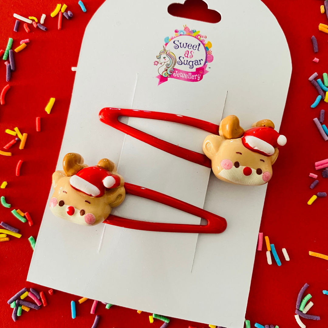Two red hair clips featuring reindeer faces complete with antlers and Santa hats