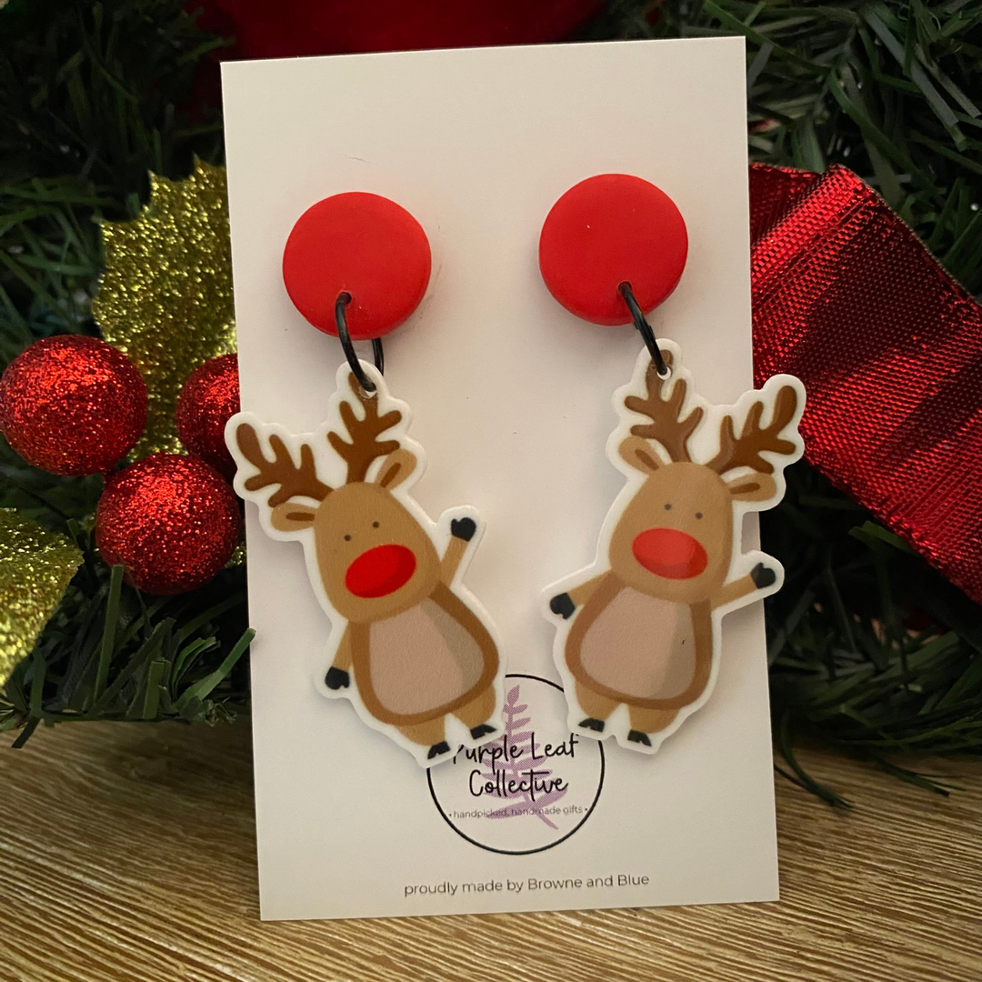 Reindeer-shaped earrings on a card with Christmas decorations in the background.