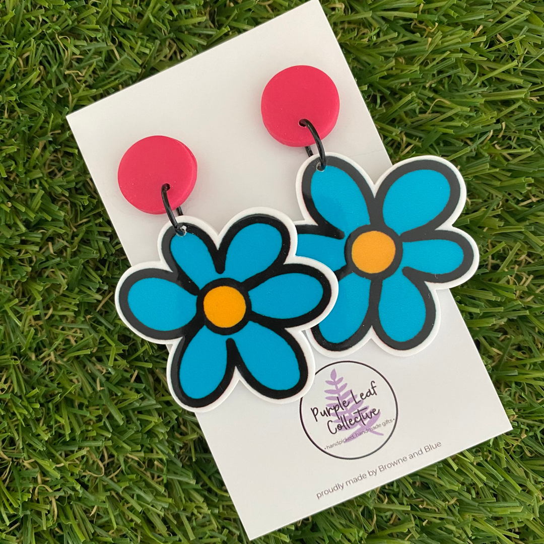 Pair of earrings featuring blue flowers with a yellow centre, set on vibrant raspberry clay tops