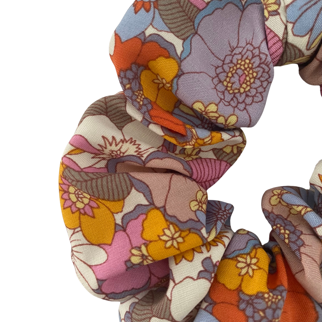 Close up view of a scrunchie featuring multicoloured retro floral pattern with pink, lilac, blue, orange and yellow blossoms.