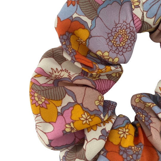 Close up view of a scrunchie featuring multicoloured retro floral pattern with pink, lilac, blue, orange and yellow blossoms.