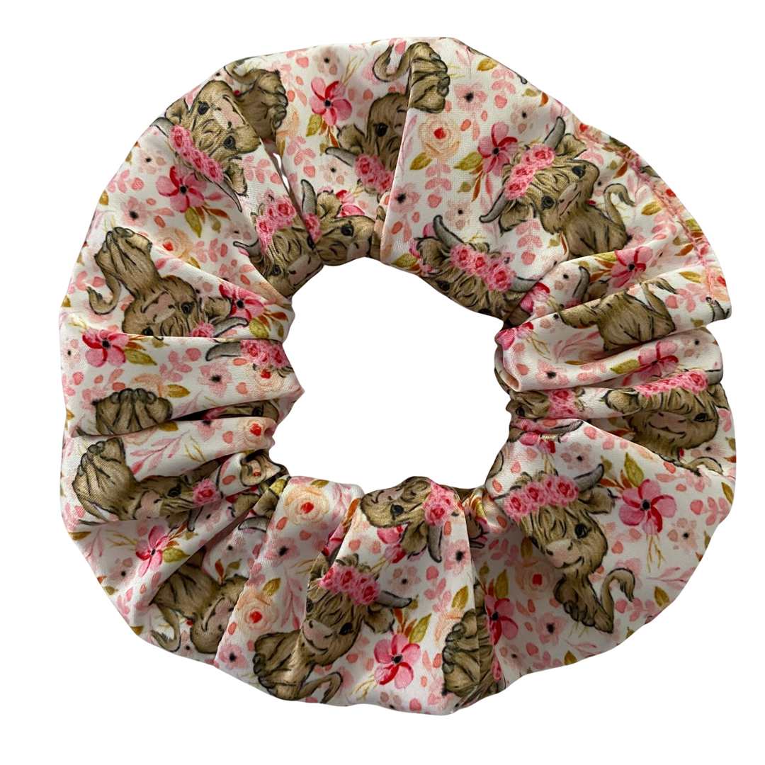 A scrunchie with highland cows and pink flowers on a white fabric.