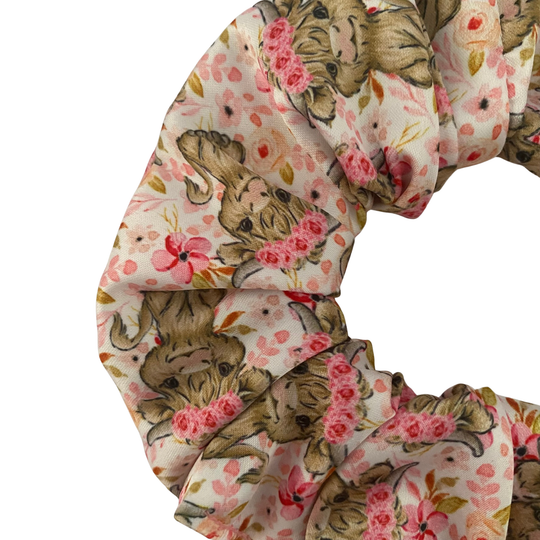 Close up view of a scrunchie with highland cows and pink flowers on a white fabric.