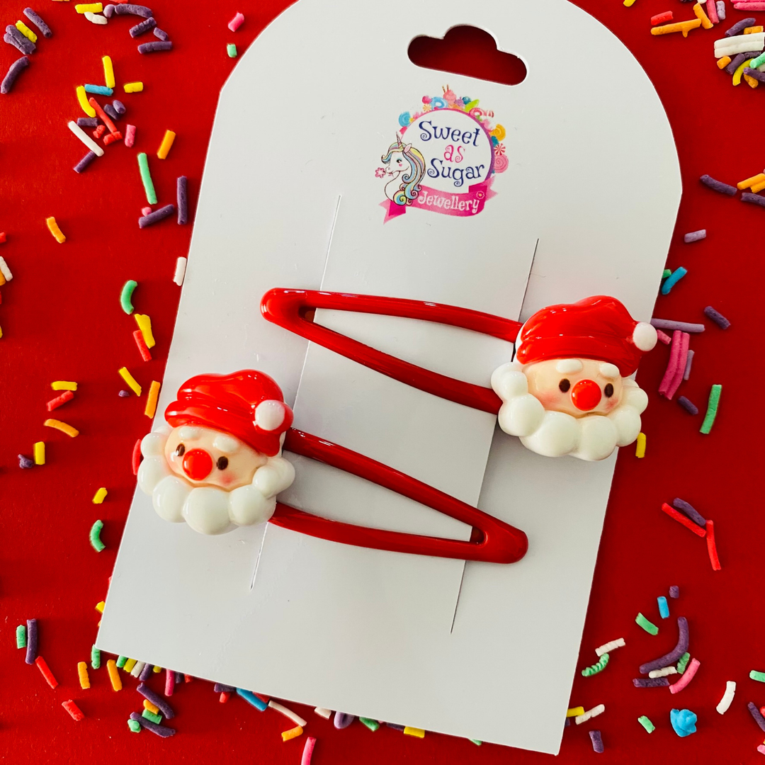 Two red hair clips featuring Santa Claus faces.