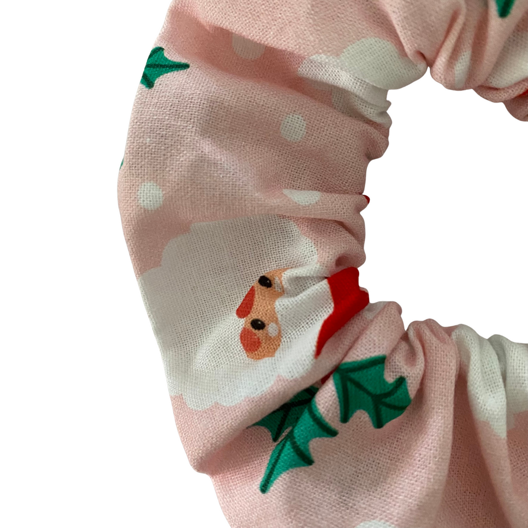 A scrunchie featuring images of Santa Claus on pink fabric.