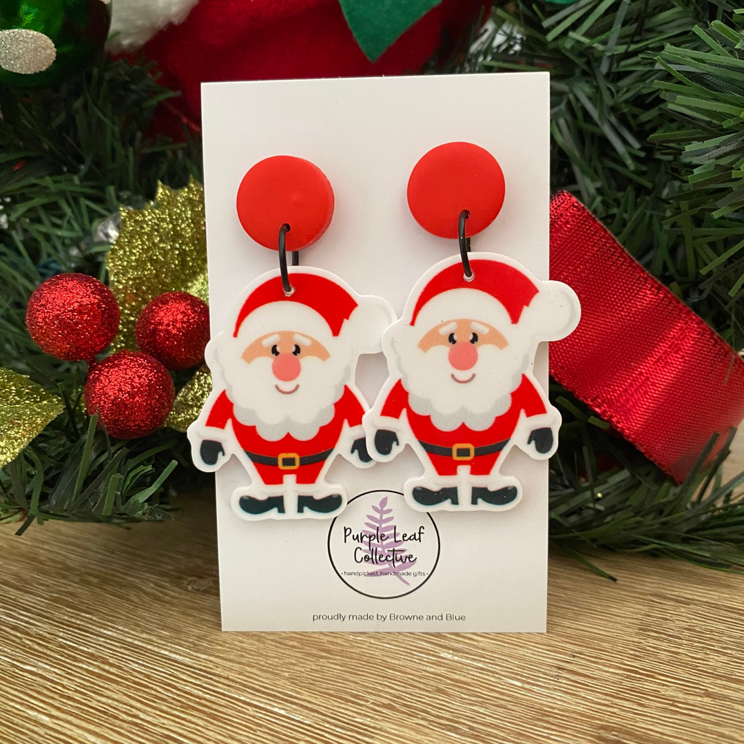 Santa Claus earrings on a card with Christmas decorations in the background.