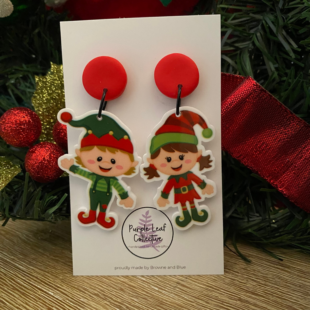 Pair of Christmas-themed earrings featuring a boy and girl elf, surrounded by festive decorations.