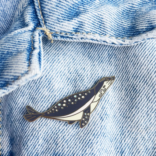 A picture of a sea lion enamel pin pinned on a denim jacket.