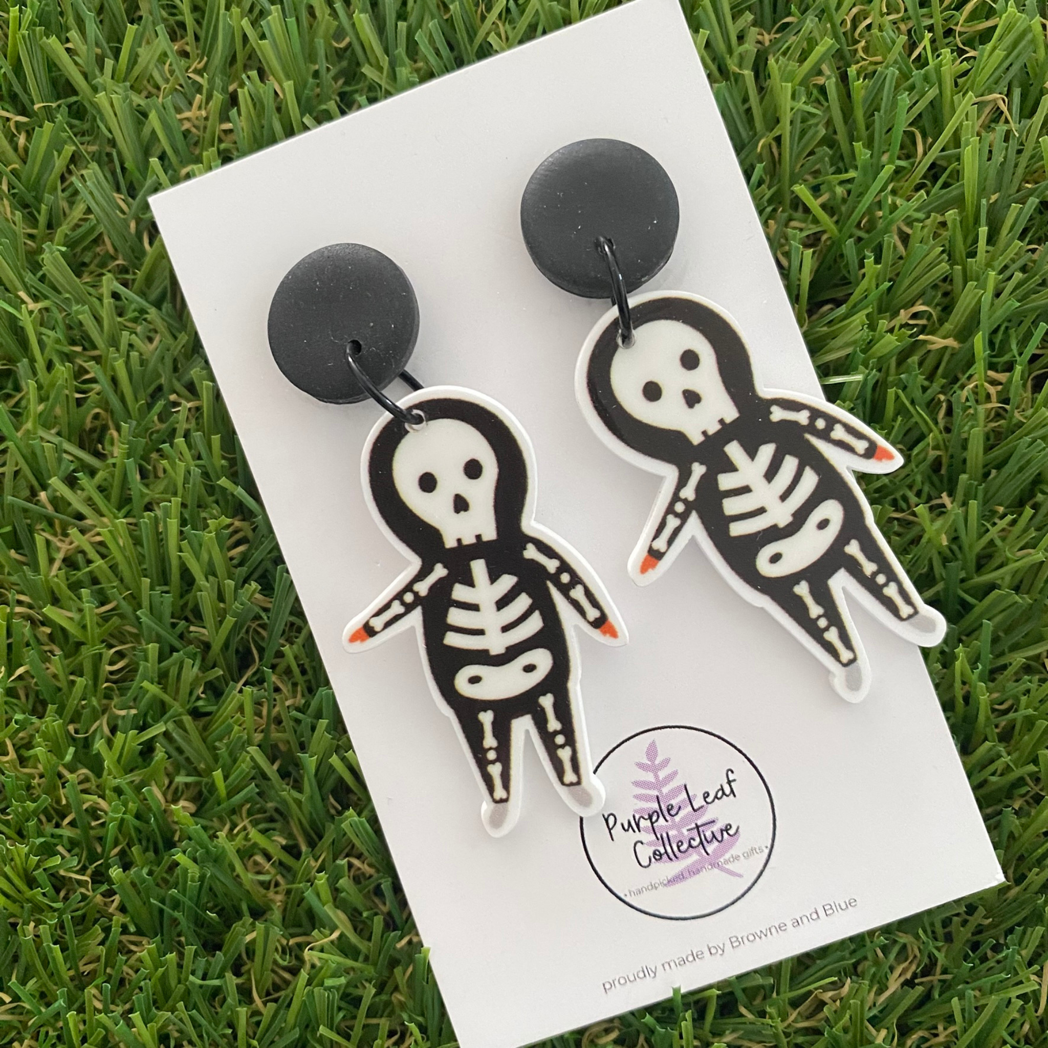 A pair of dangle earrings featuring a pair of white skeletons on black clay tops.