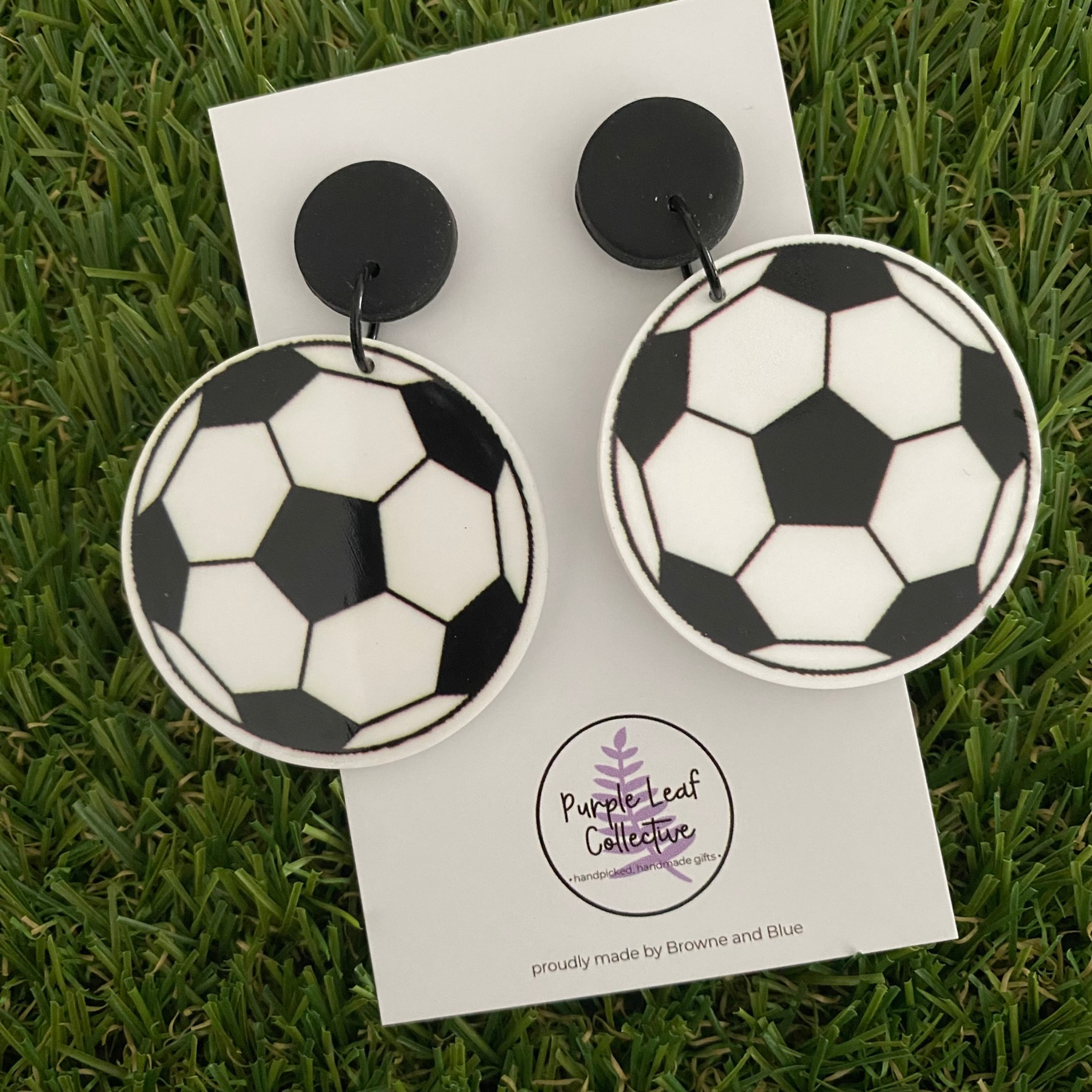 A pair of Soccer ball dangle earrings on a white backing card.