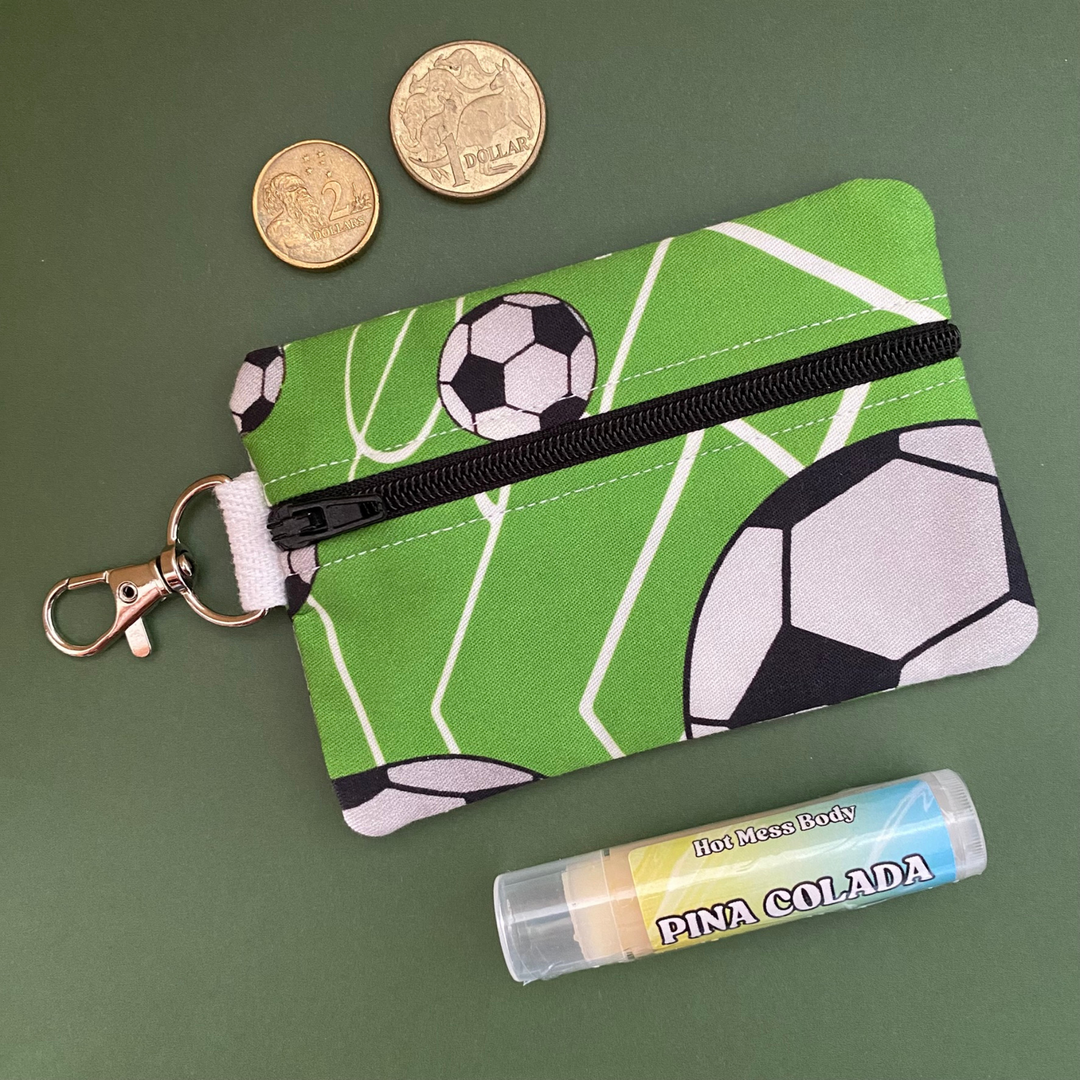 A clip coin purse with images of soccer balls on a green fabric.