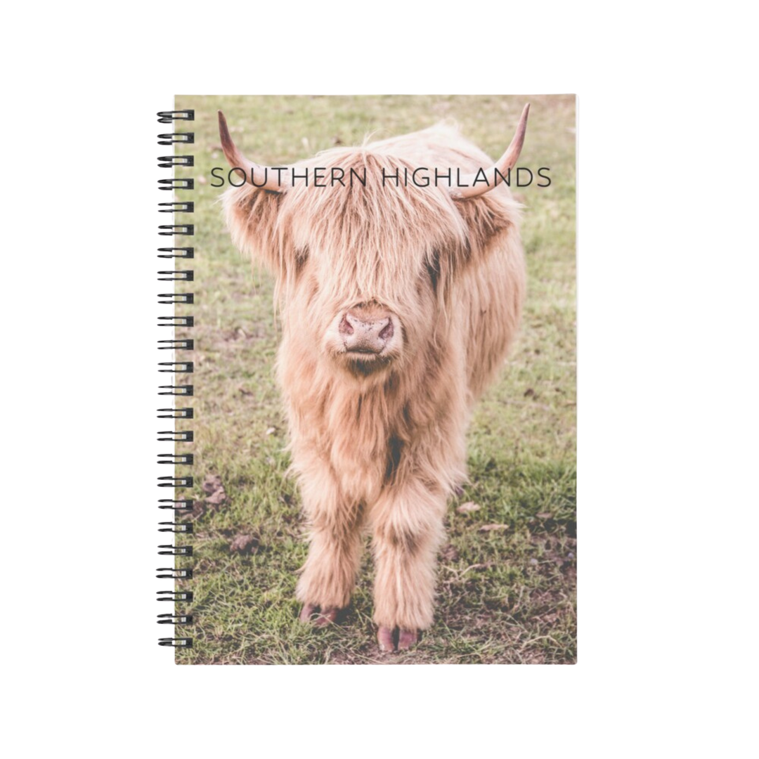 A spiral-bound notebook featuring Billy the Highland Cow with 'Southern Highlands' printed on the cover. Photography by Belinda Doyle.
