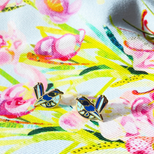 Pair of bird-shaped earrings on a colourful floral fabric background.