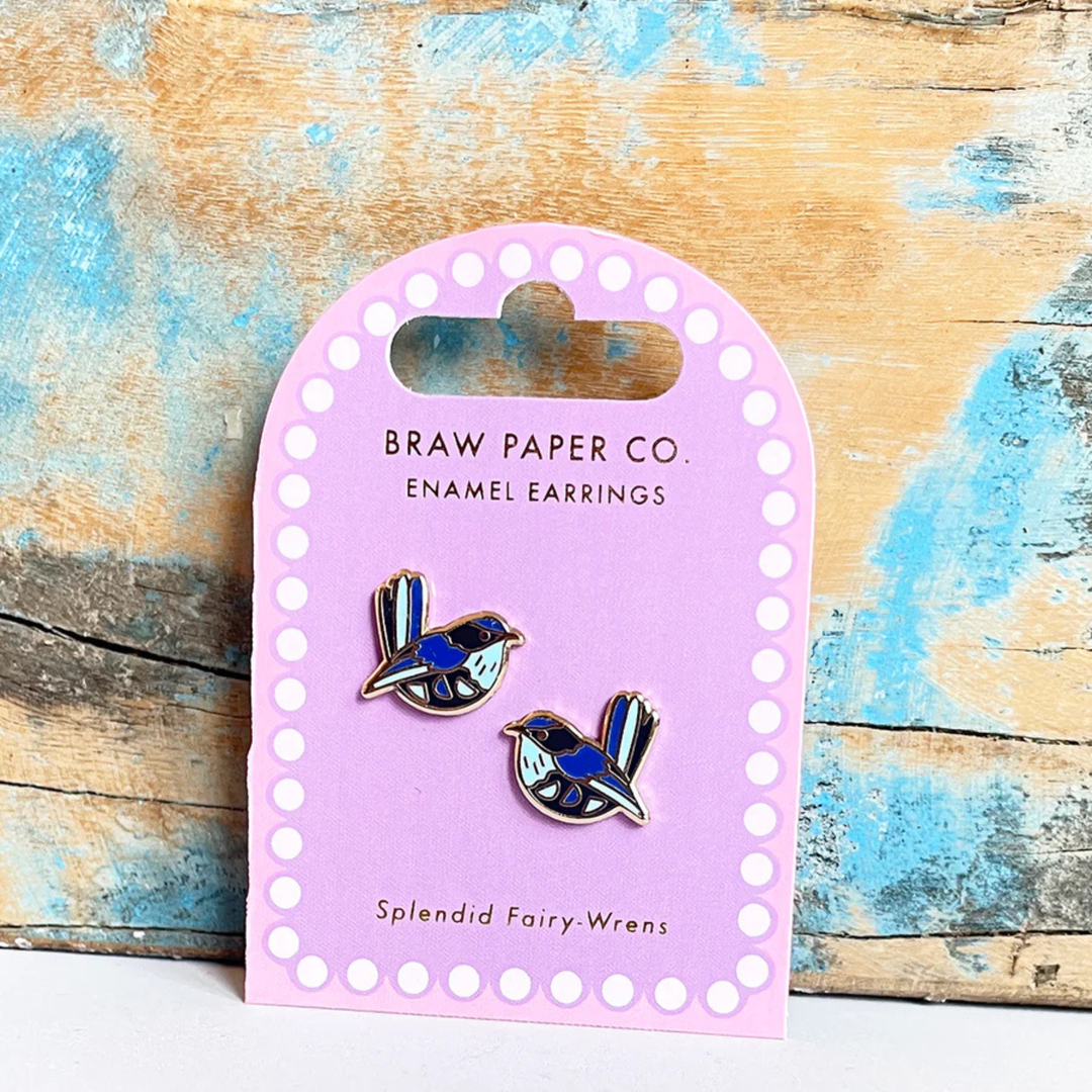 A pair of splendid fairy-wren enamel earrings on a Braw Paper Co. card against a wooden background.