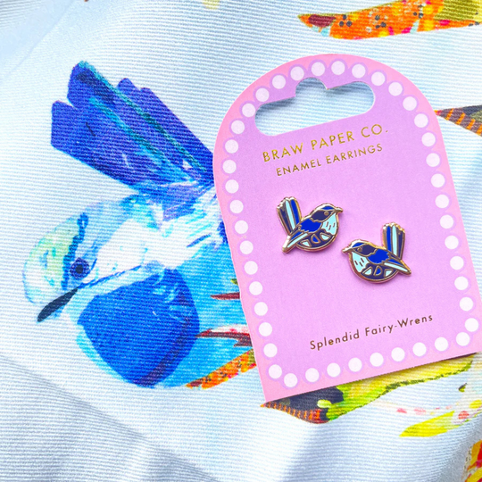 Enamel earrings on a pink card with 'Braw Paper Co.' branding, set against a colourful fabric background.