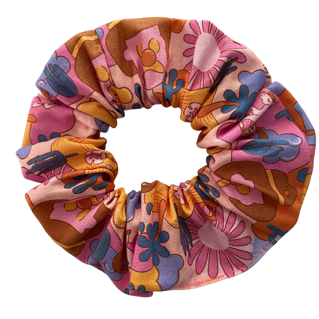 A light pink fabric scrunchie featuring a pattern of Bubble O'Bill icons, set against a background of flowers and ranch imagery.