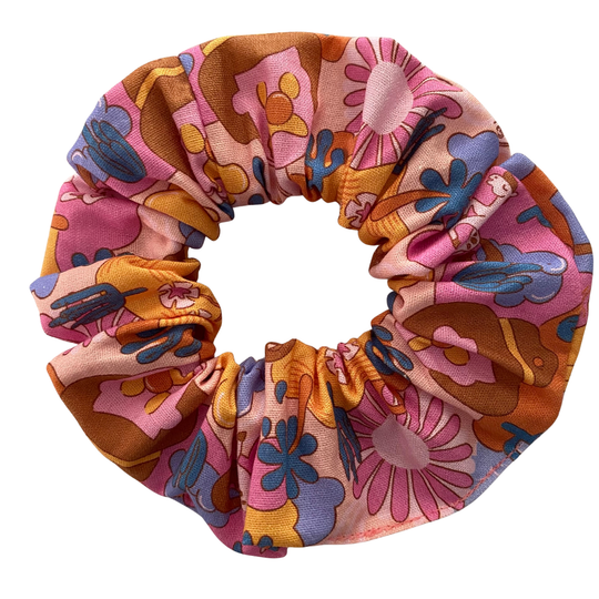 A light pink fabric scrunchie featuring a pattern of Bubble O'Bill icons, set against a background of flowers and ranch imagery.