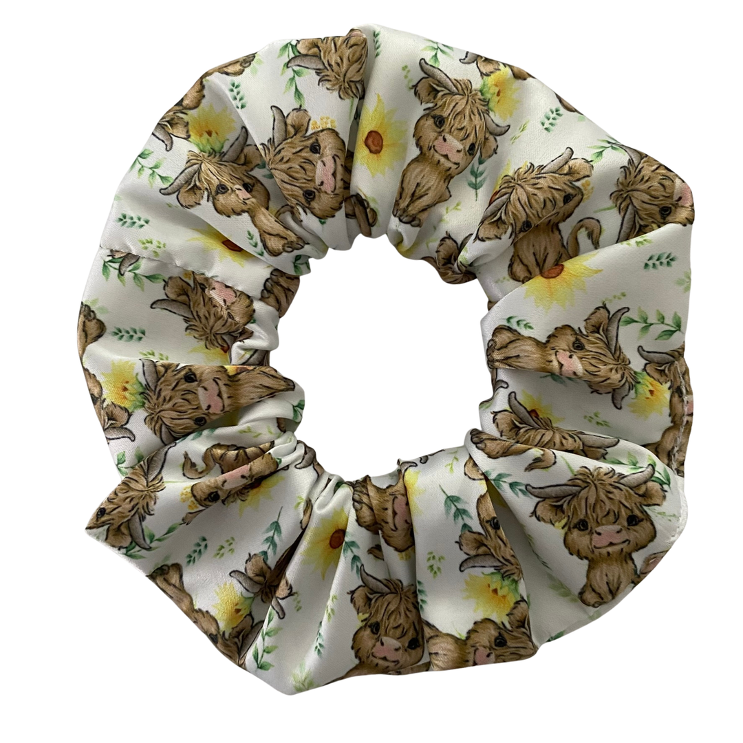 A scrunchie featuring images of highland cows and sunflowers on a white fabric.