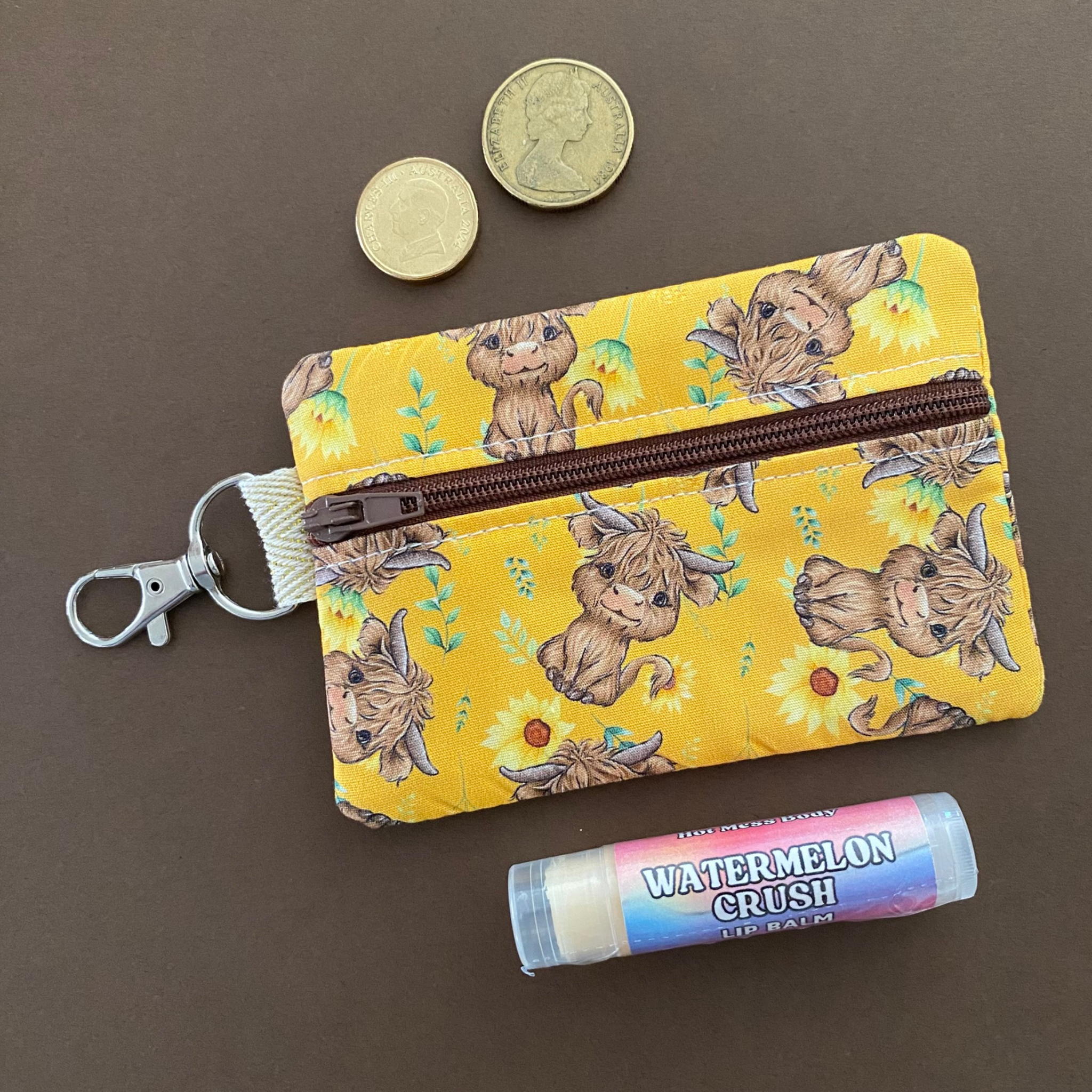 Front view of a mini pouch with images of baby highland cows and sunflowers on dark yellow fabric.