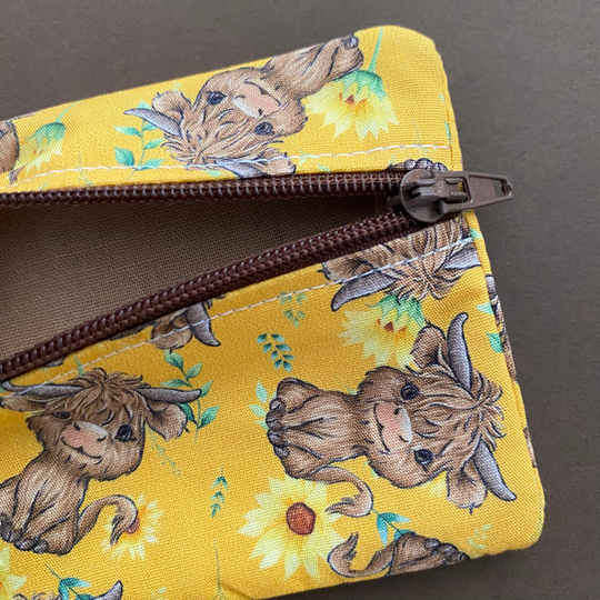 Mini pouch with images of baby highland cows and sunflowers on dark yellow fabric showing light brown lining,