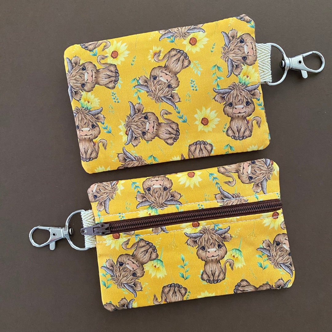 Reverse view of a mini pouch with images of baby highland cows and sunflowers on dark yellow fabric.