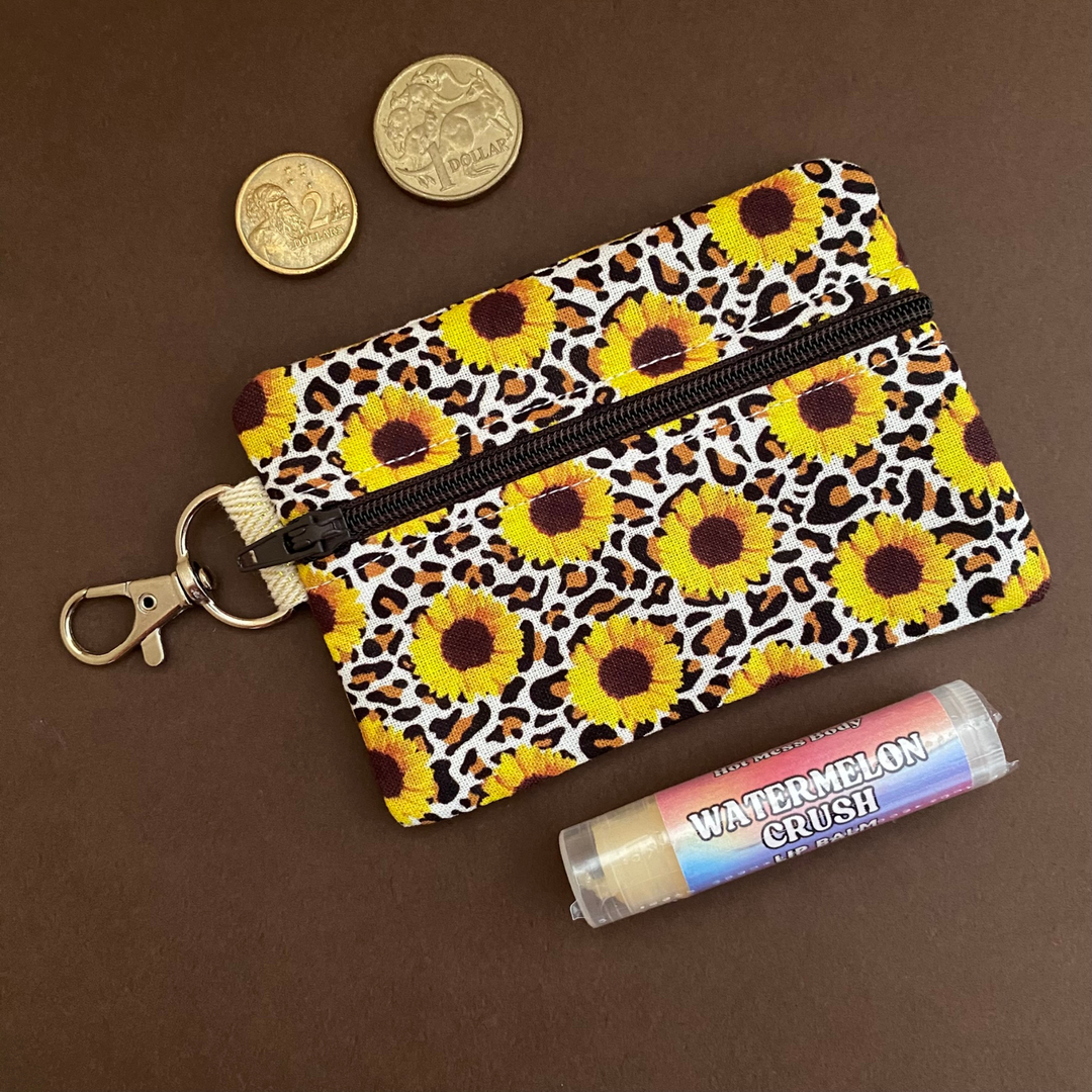A clip coin purse with images of sunflowers and leopard print on  a light brown fabric.