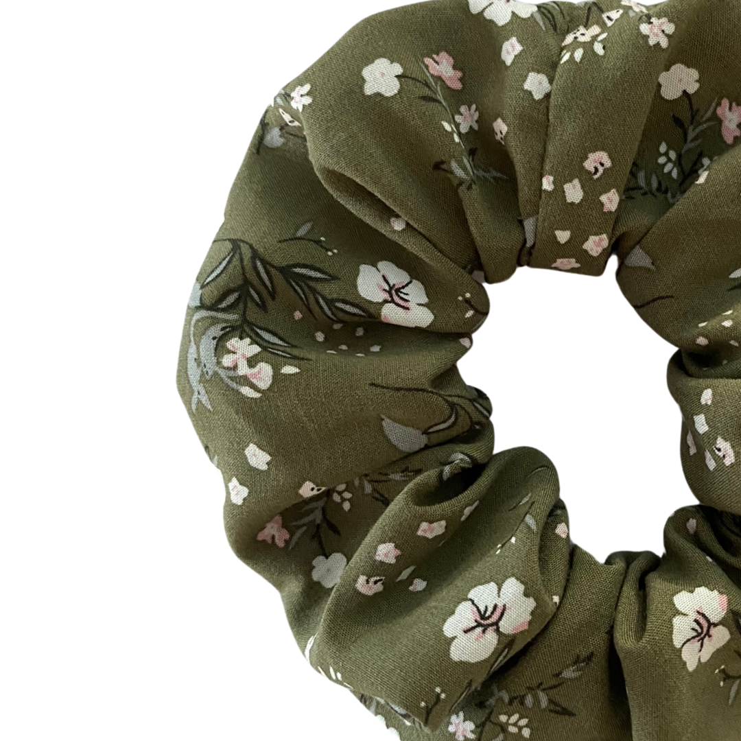 Close up view of an olive green fabric scrunchie with a delicate white and pink floral print, shown against a plain white background.