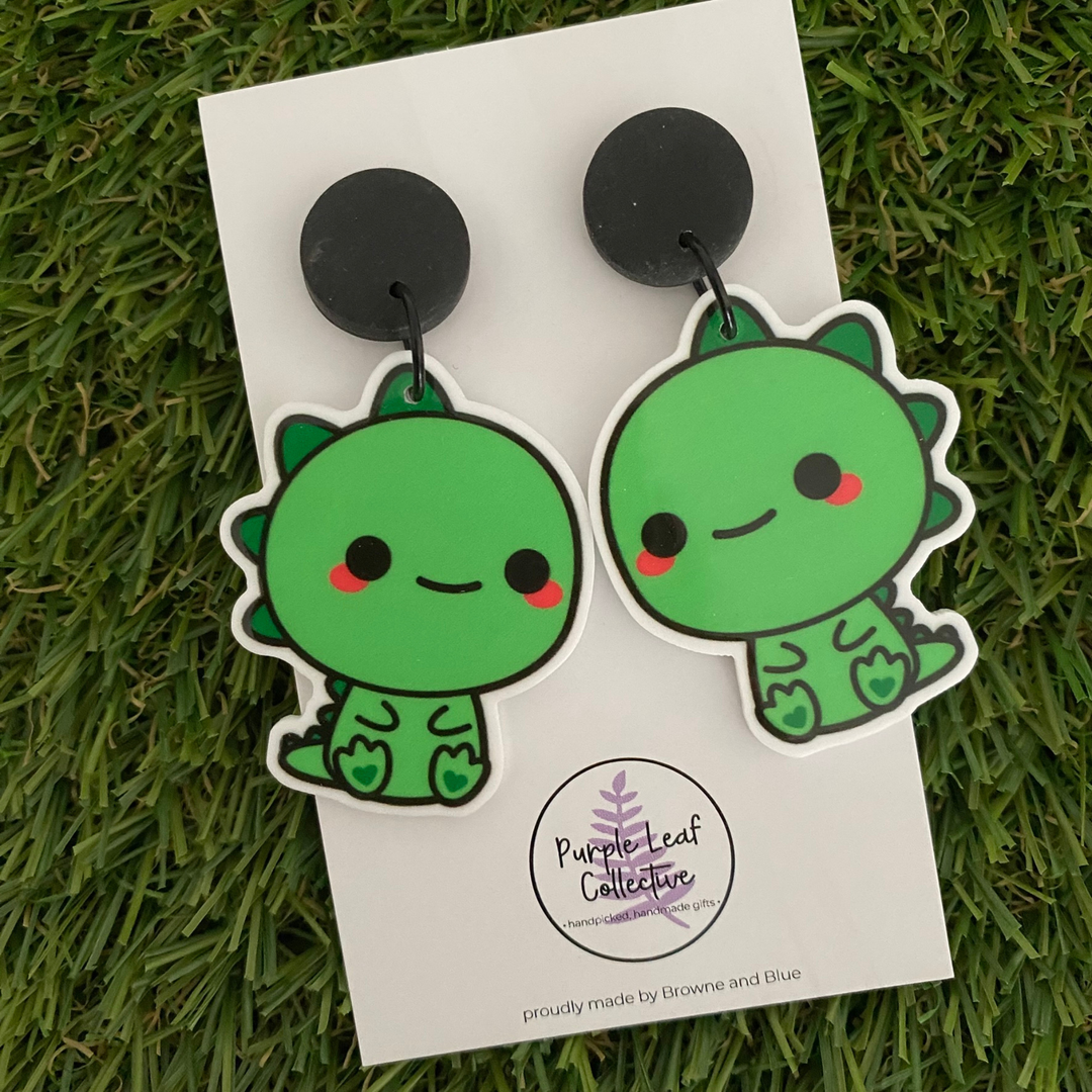 Green T-Rex dinosaur-shaped earrings set on black stud tops.