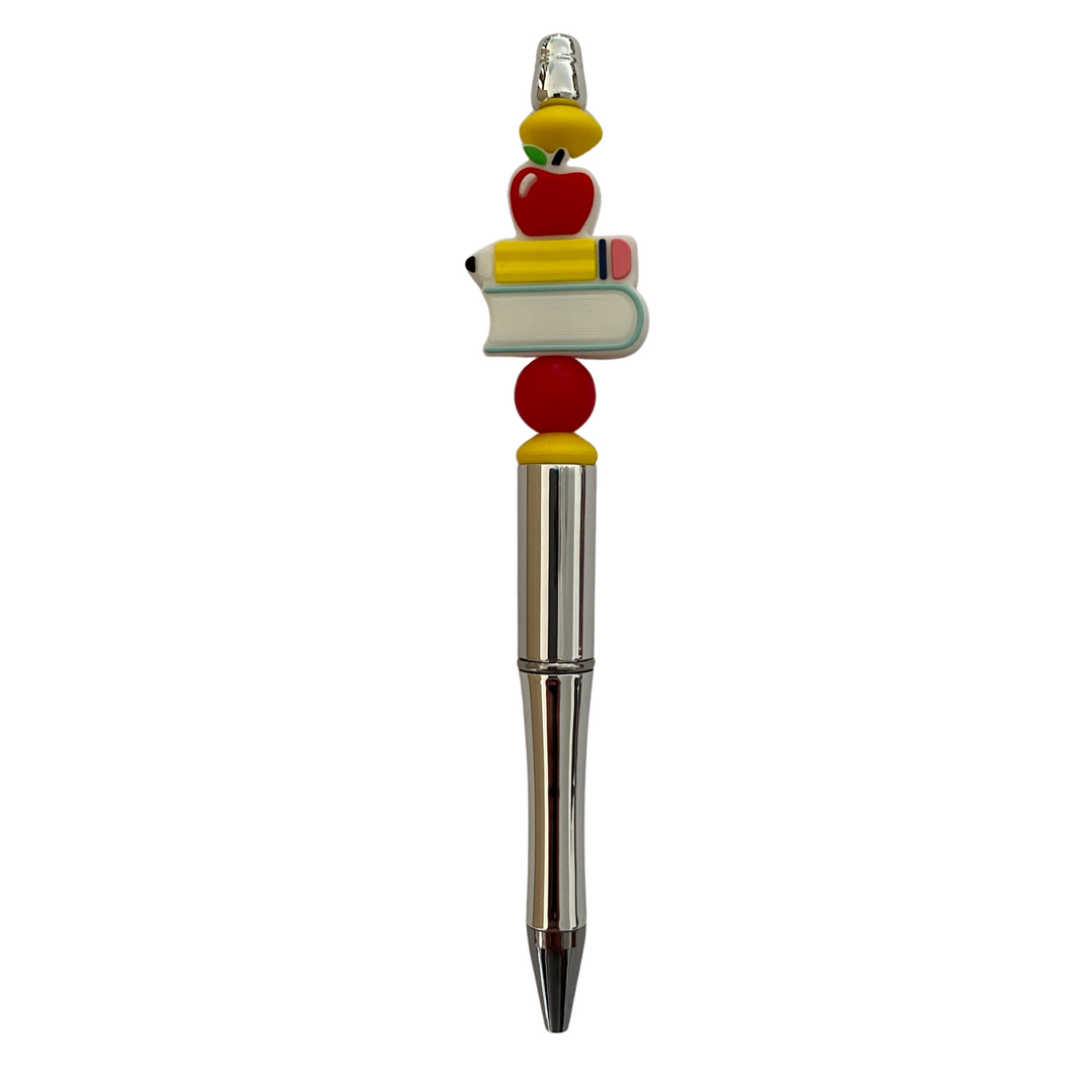 A black ink refillable pen with silicone beads shaped in a bright red apple, a classic yellow pencil and a book.
