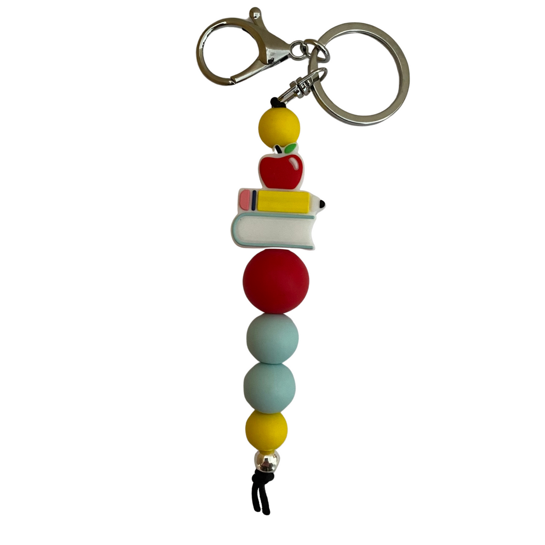 A keyring with an apple, pencil and book all stacked and other round coloured silicone beads.