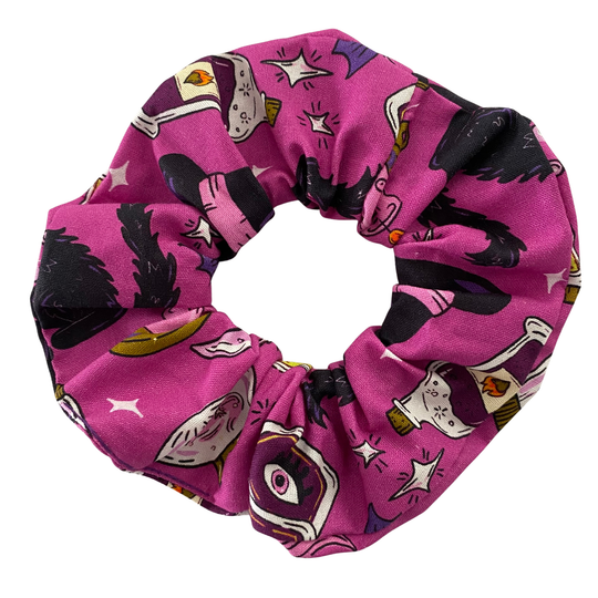Purple Halloween scrunchie with a pattern of black cats, bubbling cauldrons, potion bottles and skulls, handmade from woven cotton fabric.