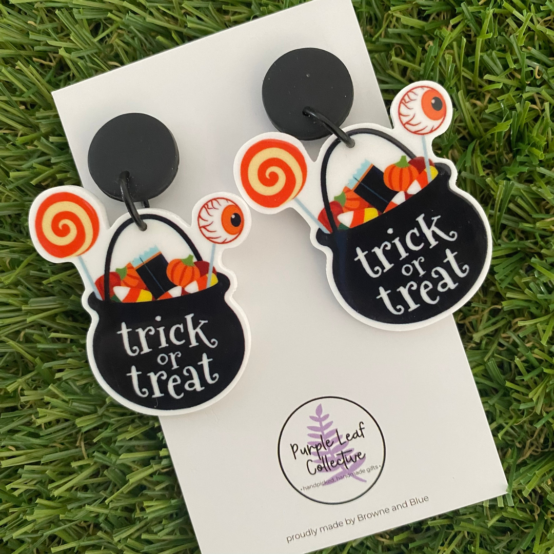 A pair of dangle earrings set on black stud tops featuring a cauldron filled with candy and the words, trick or treat.