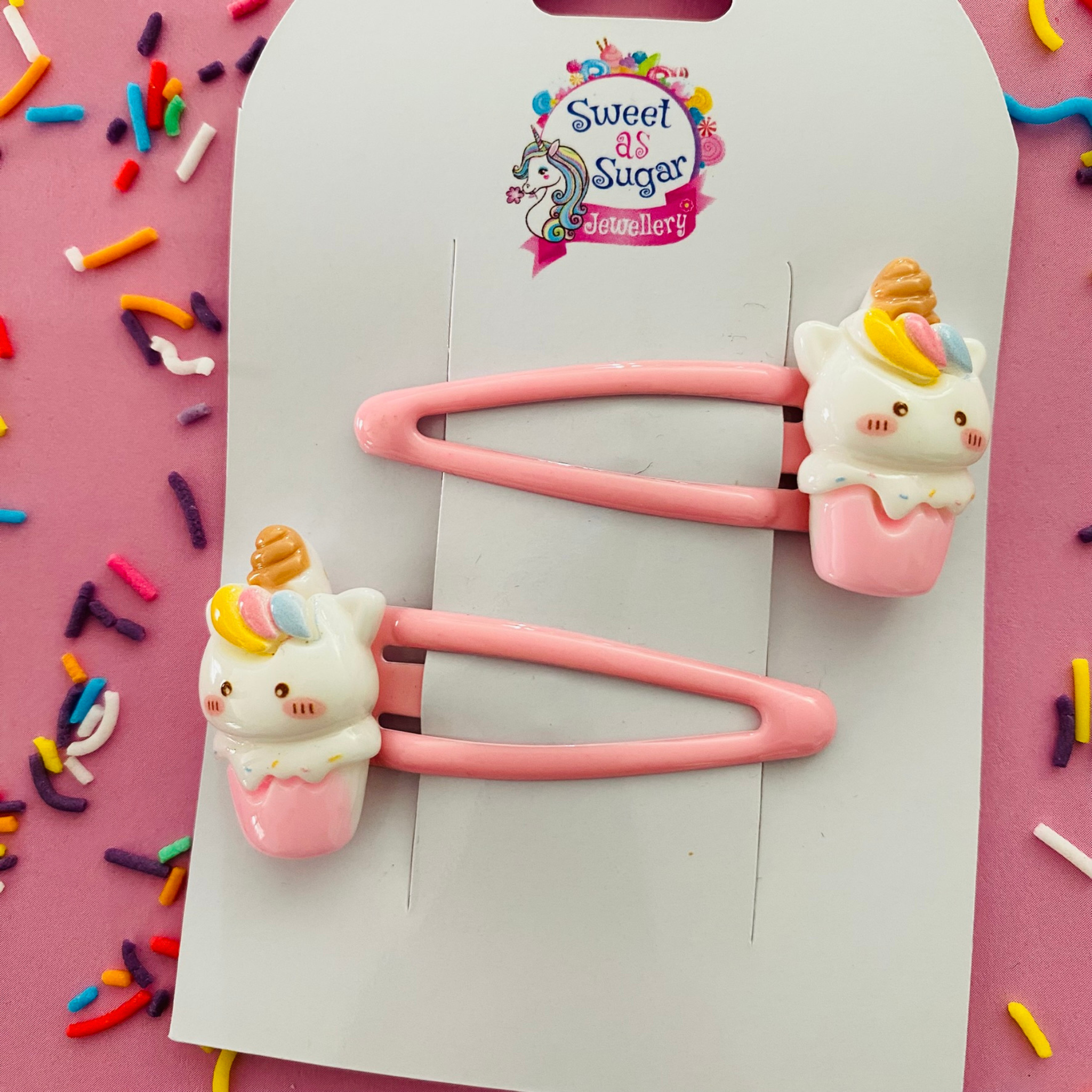 A pair of pink snap clips featuring a unicorn with a golden horn sitting in a pink cone base.