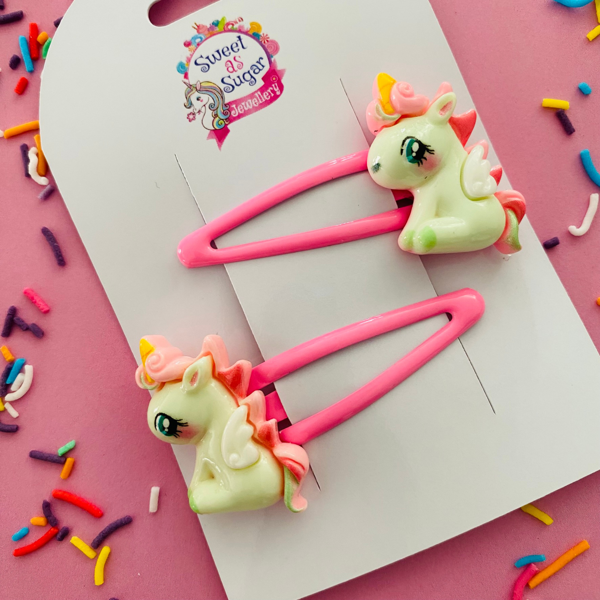 A pair of vibrant pink snap clips featuring a sitting pony with unicorn horns, mane and tail.