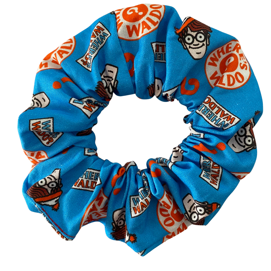 Where's Wally Head Toss Scrunchie featuring scattered images of Wally's face on blue cotton fabric, handmade with durable braided elastic.