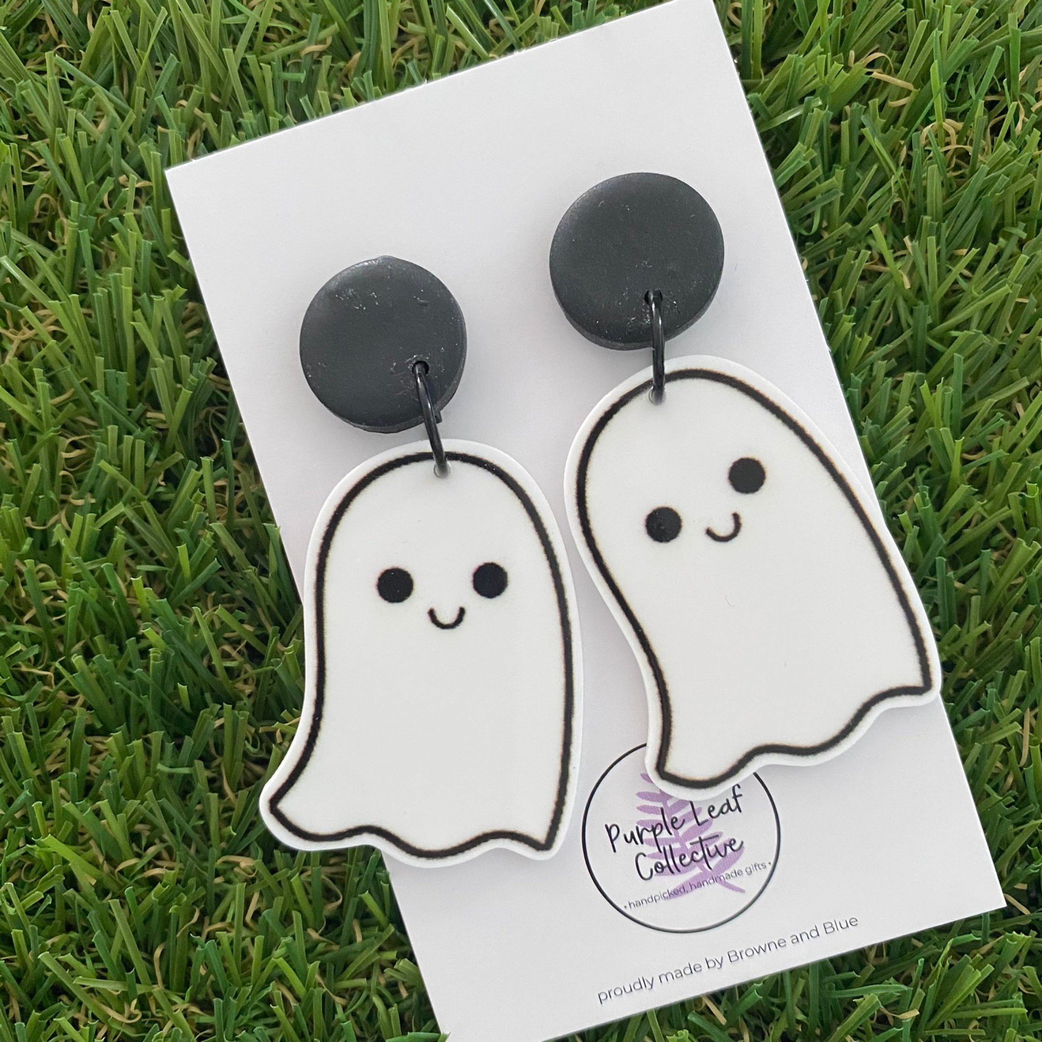 A pair of ghost-shaped dangle earrings featuring smiling faces set on black clay stud tops.