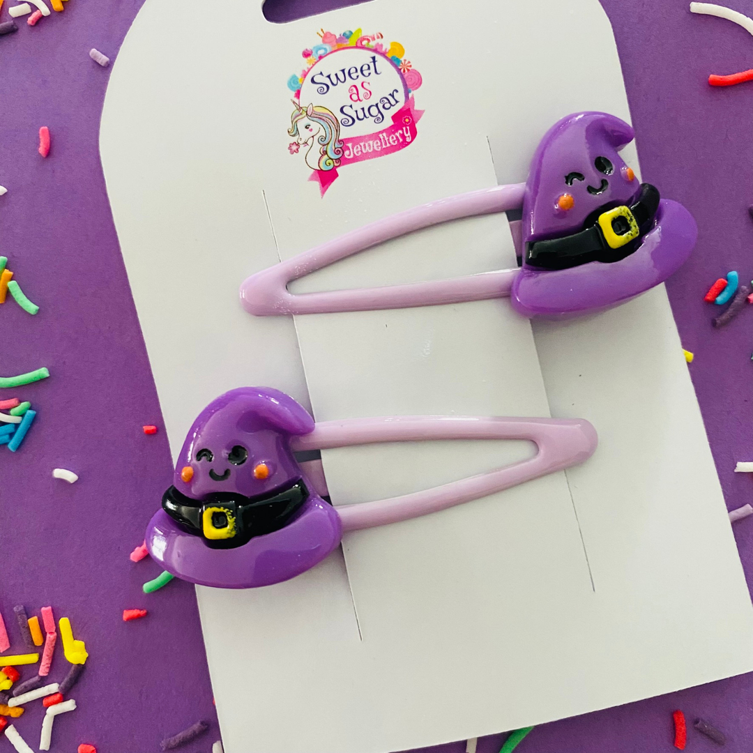 A pair of lavendar hair clips with a purple witch hat charm.